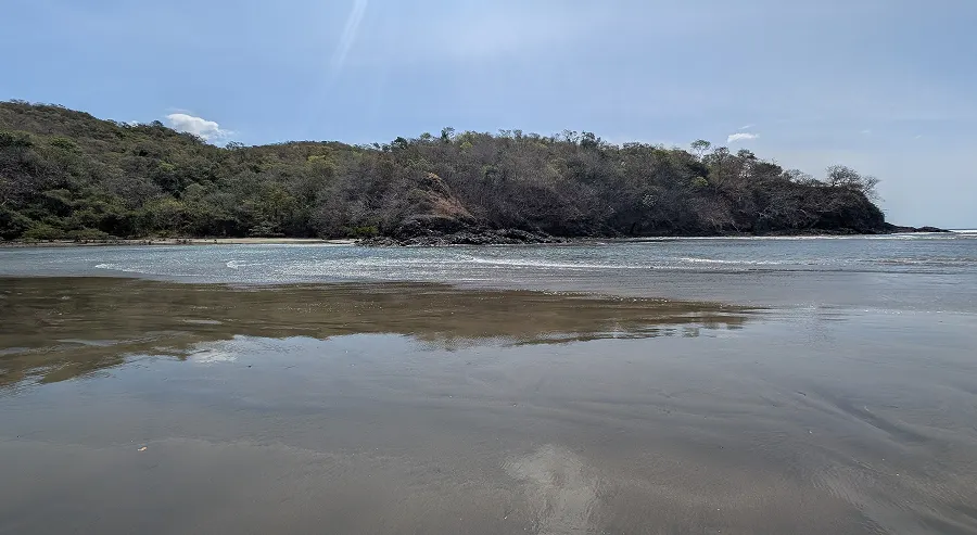 Marea baja en la playa cerca de Vista Verde, con un promontorio boscoso